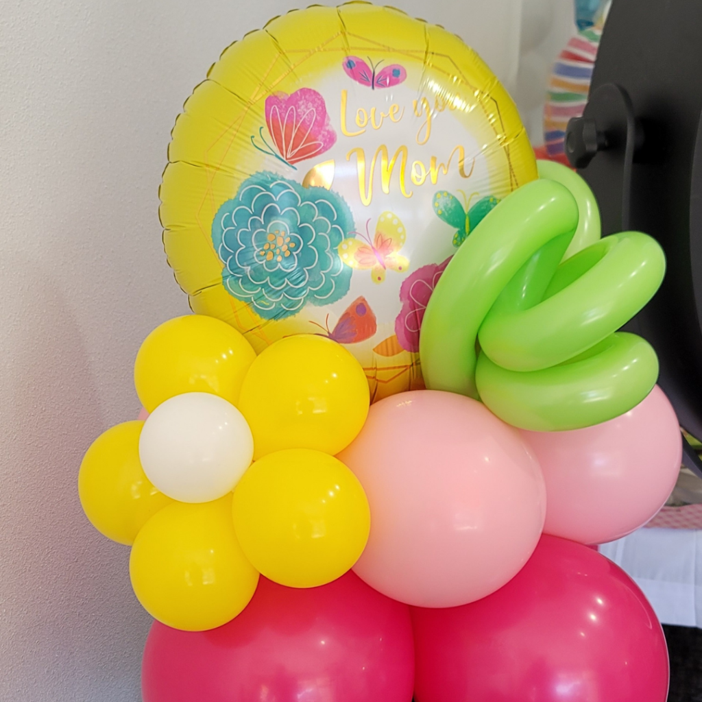 Custom-designed air-filled balloon centerpiece for Mother's Day with a 'Love you Mom' mylar balloon, artfully arranged with yellow and pink latex balloons and a creative green balloon twist.