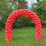 Vibrant red balloon arch standing outdoors against a green natural backdrop in Wisconsin.