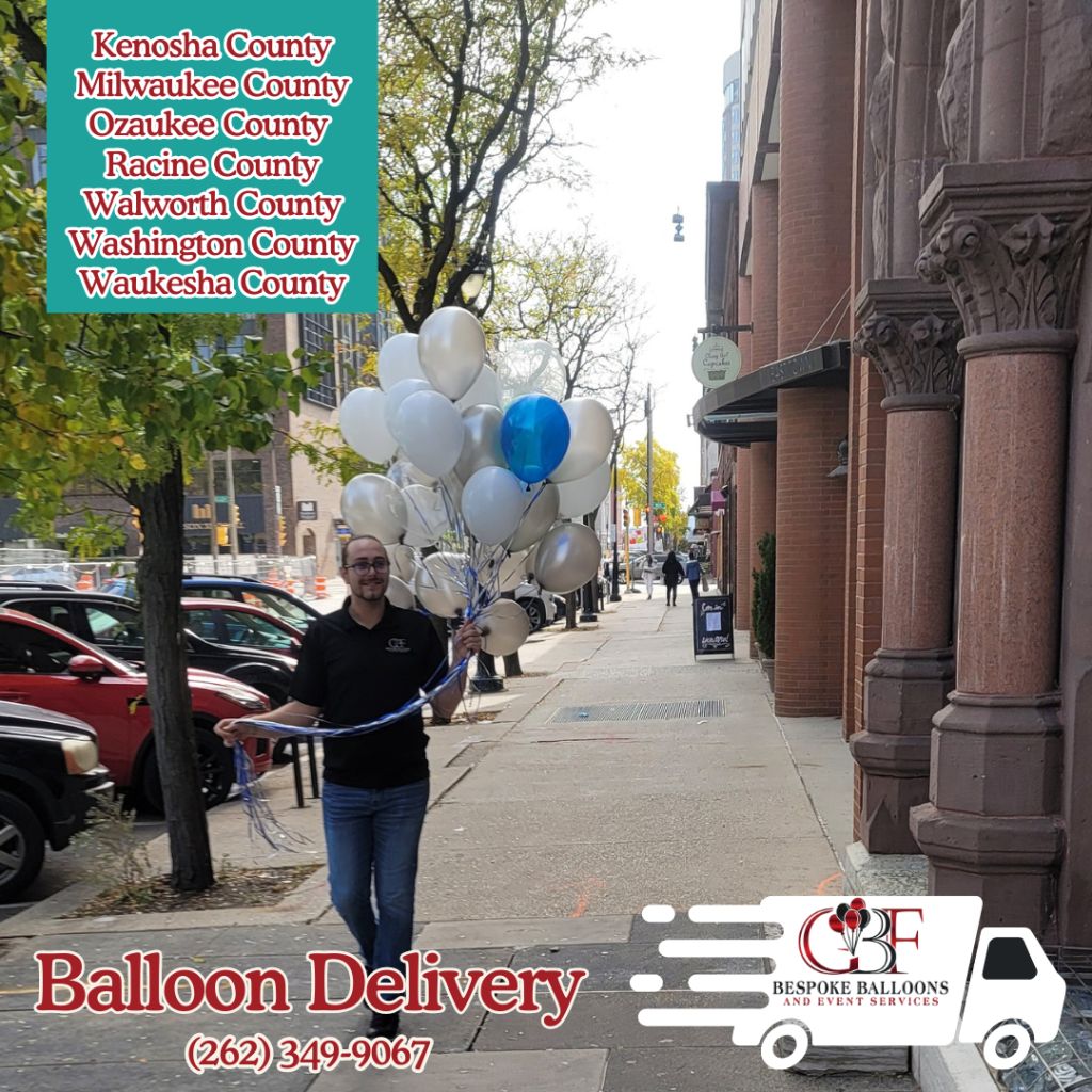 A man delivering a bunch of white and blue balloons on a city sidewalk in Southeast Wisconsin, representing GBF Bespoke Balloons and Event Services. Counties served include Kenosha, Milwaukee, Ozaukee, Racine, Walworth, Washington, and Waukesha.