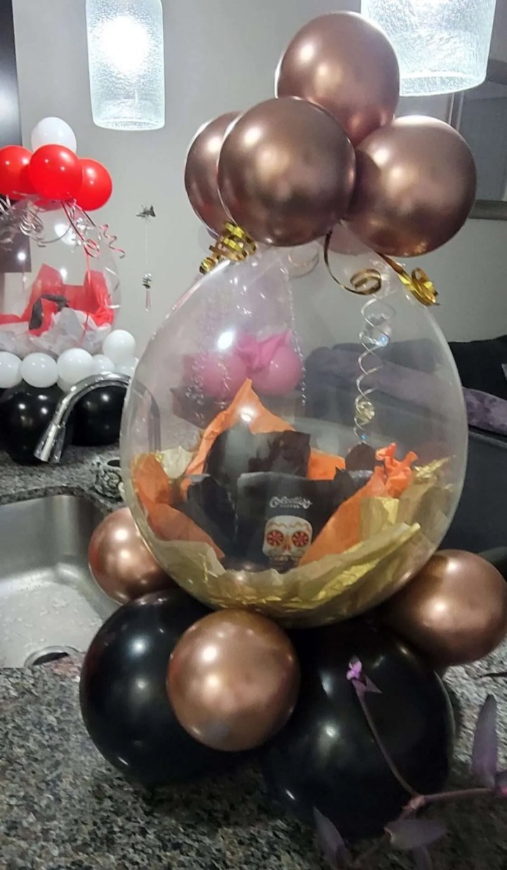 This is the coffee lover's oversized stuffed balloon by GBF Bespoke Balloons and Event Services. This Coffee lover's stuffed balloon has colectivo coffee inside of an 18" stuffing balloon. The stuffed balloon is on a balloon base of black and rose gold balloons with gold and orange tissue paper inside the balloon to compliment the colors on the Colevtivo Coffee bag.